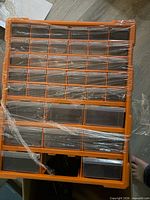 Front view of orange organizer showing rows of clear drawers covered in plastic film