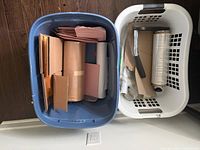 Two laundry bins holding bubble mailers, cardboard flats, stretch wrap dispenser and film