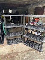 Two black plastic 4-tier shelving units standing side by side in garage