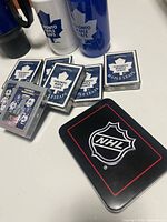 Lot overview showing travel mug, water bottle, multiple sealed playing card decks and NHL tin