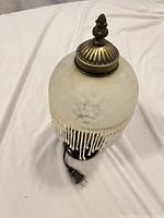 Side view showing glass globe, beaded fringe, metal top finial and power cord