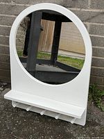 Front view showing round mirror set into white rectangular frame with shelf and five hooks