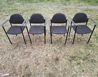 Four matching black cushioned office chairs arranged side by side outdoors