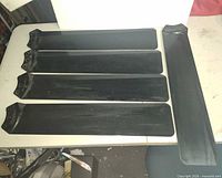 Five black ceiling fan blades laid out on table