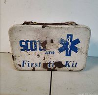 Front of metal first aid kit showing blue graphics and rust wear