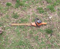 Full view of Craftsman orange hedge trimmer lying on grass
