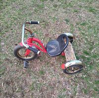 Left side view of red Schwinn tricycle showing frame, wheels and seat