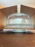 Glass cake dome resting on footed plate inside open box