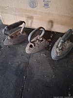 Front view of three cast iron hand irons showing handles and rusted tops