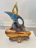 Front view of gold and blue ceramic decanter with grape motif
