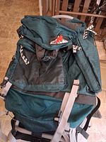 Front view of dark green K2 external frame backpack on floor