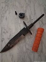 Blade, orange handle, pommel piece and screw on surface