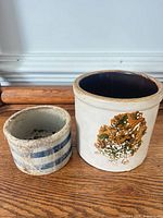 Two stoneware crocks side by side showing size difference and design details