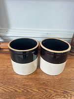 Front view of both stoneware crocks showing brown glazed band and cream lower portion