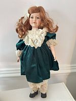 Full view of porcelain doll standing on table wearing green velvet dress, undergarments visible, black shoes