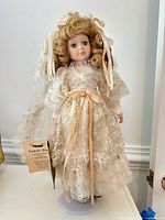 Full front view of Seymour Mann porcelain doll on stand showing dress, hair, veil, tag