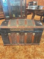 Front view showing dome lid, embossed metal panels, metal straps and brass hardware