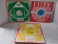 Three vinyl records in World Enterprise Disco 45 sleeves, green, red and yellow variants