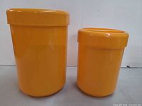 Two orange canisters side by side showing relative sizes and lids