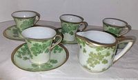 Full set: four cups, four saucers, one creamer showing pattern and trim