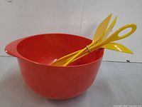Side view of red Rosti mixing bowl with four yellow utensils inside