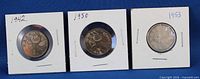 Front view of three silver Canadian quarters dated 1942, 1950, 1953 in cardboard holders