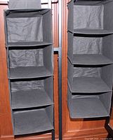 Two black fabric hanging closet organizers side by side showing shelves