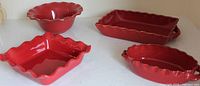 Top view of four red stoneware pieces displaying shapes and scalloped edges