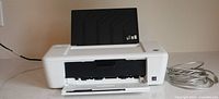 Front view of HP DeskJet 100 printer with paper tray open and USB cable beside unit