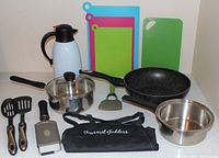 Overall lot showing all cookware, utensils, carafe, cutting boards, apron
