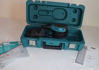 Open Makita case showing sander, dust bag, sandpaper sheets and manuals