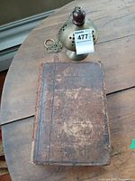 Book closed showing worn leather cover alongside brass censer with chain and wood finial
