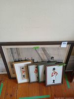 All five framed prints leaning against wall: one large naval scene, four soldier portraits