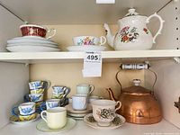 Shelf view showing assorted teacups, saucers, teapot, copper kettle