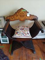 Front view of armchair showing marquetry backrest, curved slat sides, X-frame base and cushion