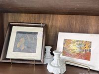 Overall view of both framed artworks and pair of milk glass candle holders on shelf