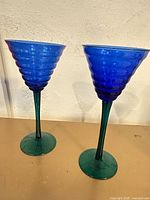 Two cobalt blue ribbed cocktail glasses with green stems and bases