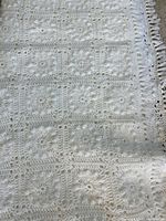 White crocheted bedspread showing square motif and fringe