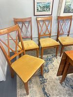 Four wood dining chairs with yellow velveteen seats and lattice backs