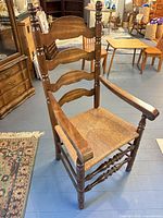 Front angled view showing ladderback design, rush seat, arms, turned legs