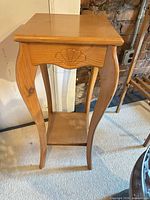 Full view of oak plant stand showing top, carved shell apron, curved legs and lower shelf