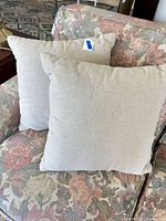 Two beige square pillows displayed on floral armchair
