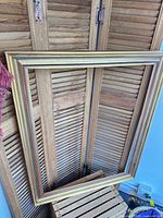 Full view of rectangular gold wooden frame leaning against shutter backdrop