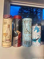 Front view of four cylindrical wine gift boxes standing side by side showing full designs
