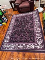 Full view of purple, black and white patterned rectangular area rug on hardwood floor
