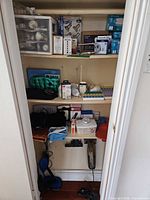Closet shelves showing bulk of listed items including bulbs, baby monitor box, heat packs, pill organizer and Hoover vacuum at bottom