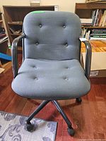 Front view of chair showing upholstery, arms, button tufting, casters