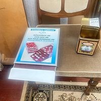 Tin of coins next to Lighthouse MB coin box on chair