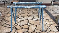 Two blue metal folding sawhorses standing on patio