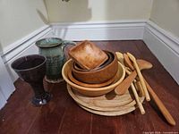 Group view of wooden platters, bowls, square dish, spoons, ceramic goblet, and pitcher